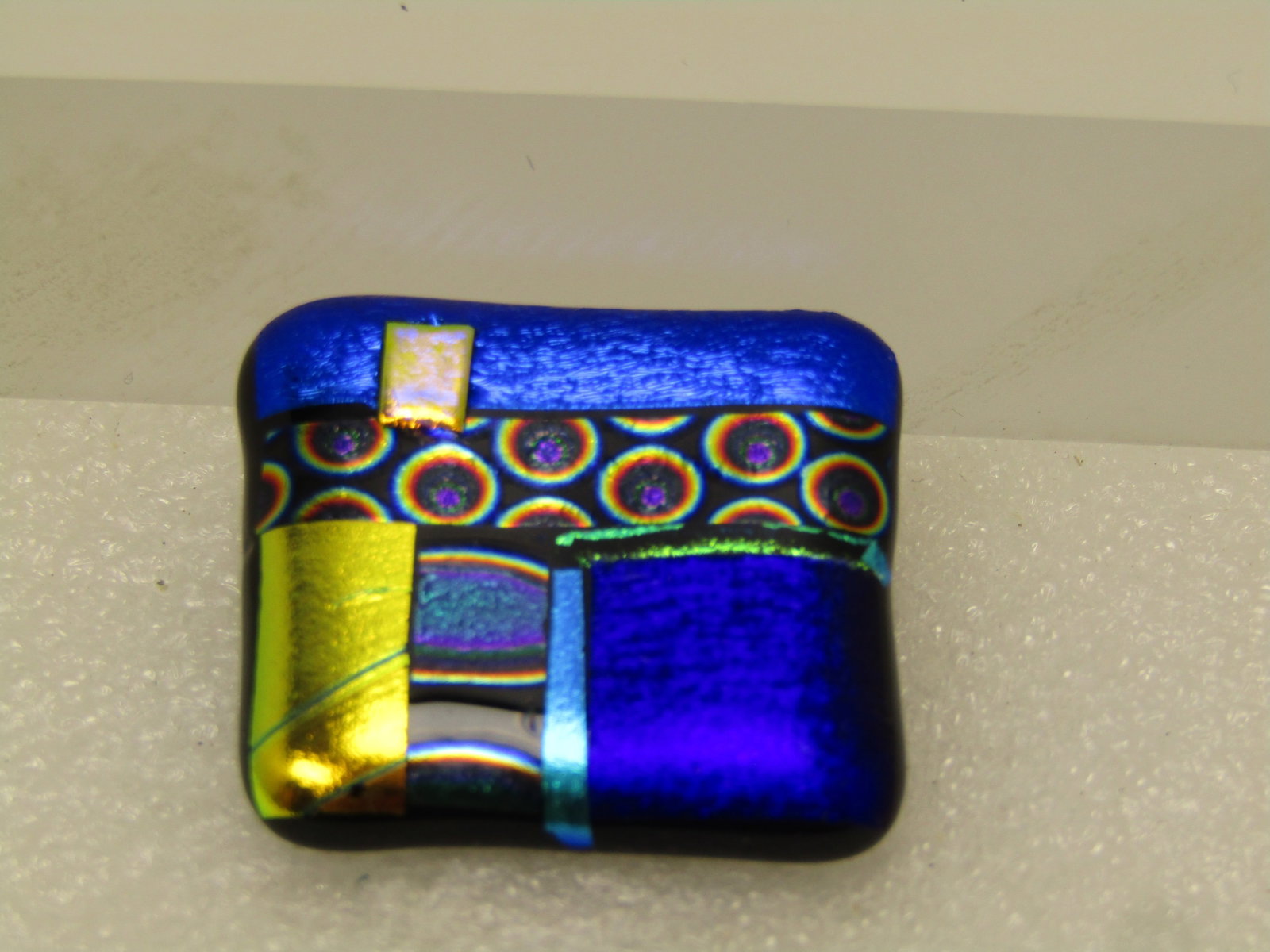 Vintage Dichroic Fused Glass Brooch, Vibrant Colors, 1980's-1990's: Vintage Dichroic Fused Glass Brooch, Vibrant Colors, 1980's-1990's. This is appx. 1.25" square. Black glass base with the dichroic accents done in a patchwork design with foiling and shimmery blue, pu