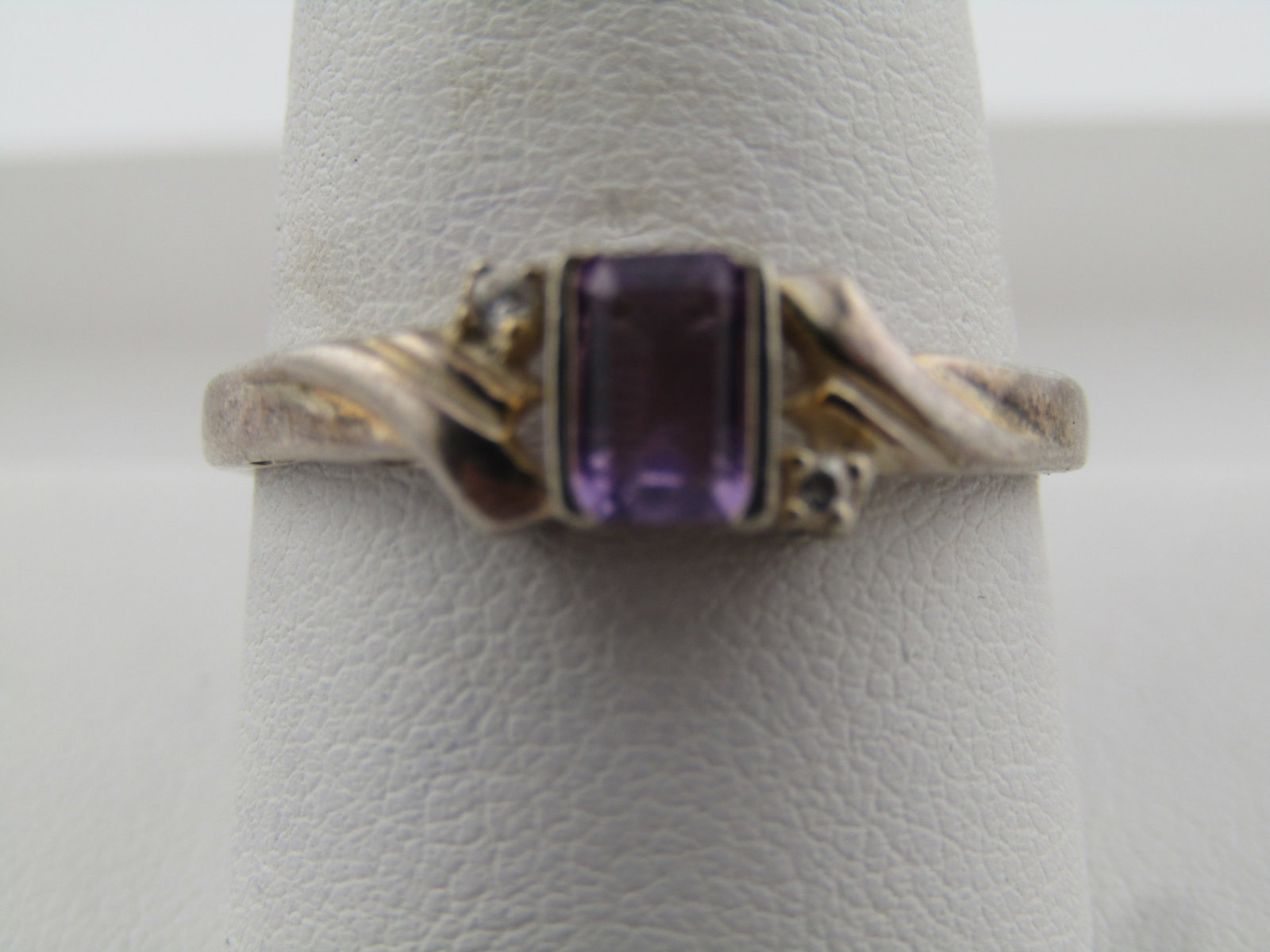 Vintage Avon Amethyst CZ Ring, Sz. 10.5, 1970's-1980's: Vintage Avon Amethyst CZ Ring, Sz. 10.5, 1970's-1980's. This has an appx. 5.5mm by 4.5mm rec tangular amethyst set with side channel bezel and open on the short ends. There is a single clear CZ on eac