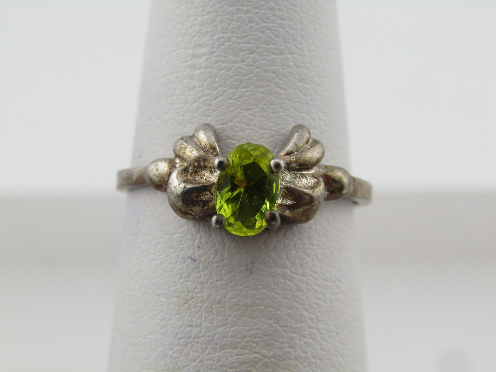 Silver Plated Green Stone Bow Ring, Sz. 6, 1980's: Silver Plated Green Stone Bow Ring, Sz. 6, 1980's. This has a green peridot colored stone - glass - that is oval 5.8mm by 3.9mm. Set with four prongs at the center of a blow that sits lower. The ring
