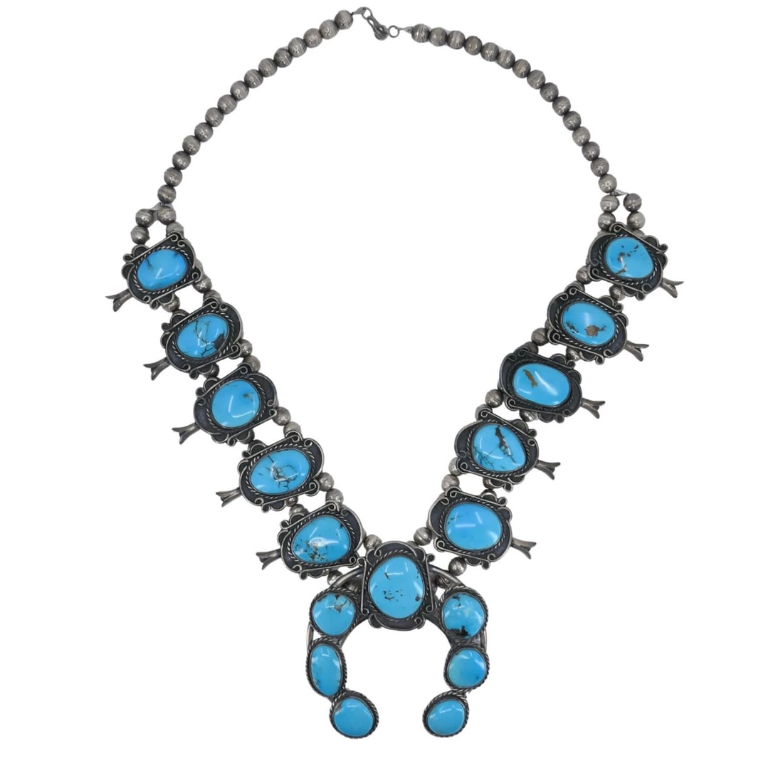 Navajo Native Indian Sterling Silver Turquoise Squash Blossom Necklace: KL JUTO This striking Navajo squash blossom necklace is crafted in sterling silver and set with vivid blue turquoise cabochons, each showing natural matrix that highlights the stone's character. The n
