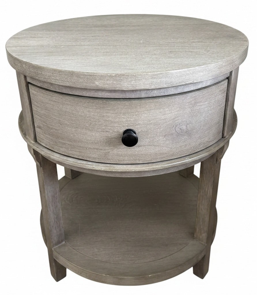 Contemporary Round Wood Nightstand with Drawer and Shelf: A contemporary round nightstand featuring a single drawer with a black pull and an open shelf below. The nightstand is constructed from wood with a light, distressed grey wash finish. Its compact