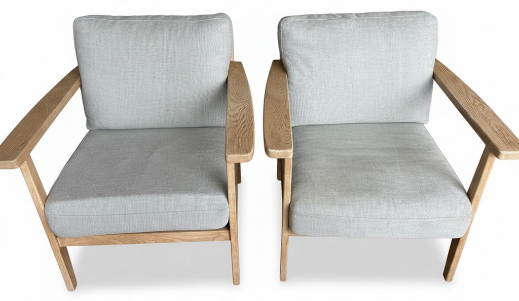 Pair of Modern Light Wood and Upholstered Armchairs: A pair of modern armchairs featuring light-toned wooden frames and light grey upholstered cushions. The design is characterized by clean lines and an open back with vertical slats. The armrests are
