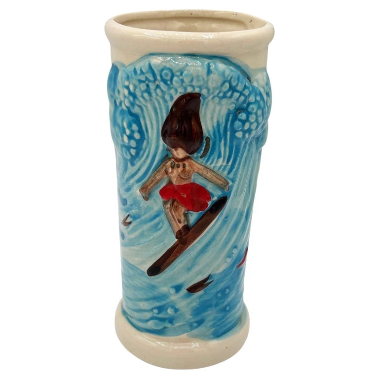 1980 Trader Dick's Casino Surfer Hula Girl Riding Wave Blue Ceramic Tiki Mug: Mid-century style Trader Dick's Casino Surfer Hula Girl Riding Wave Blue Ceramic Tiki Mug. The mug features a central figure is depicted in mid-ride on a surfboard, wearing a vivid red wrap against a 