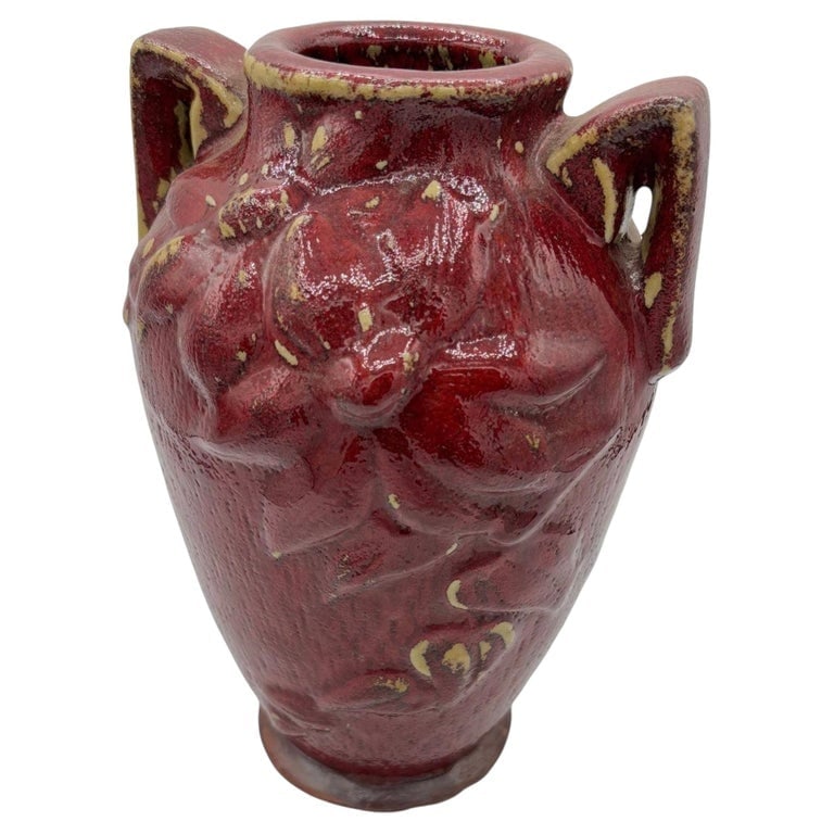 Red Art Pottery Vase with Dual Handles and Sculpted Floral Relief: Striking and richly textured, this vintage art pottery vase features a deep oxblood red glaze accented with warm golden undertones along the rim and handles. The sculpted body showcases bold floral an
