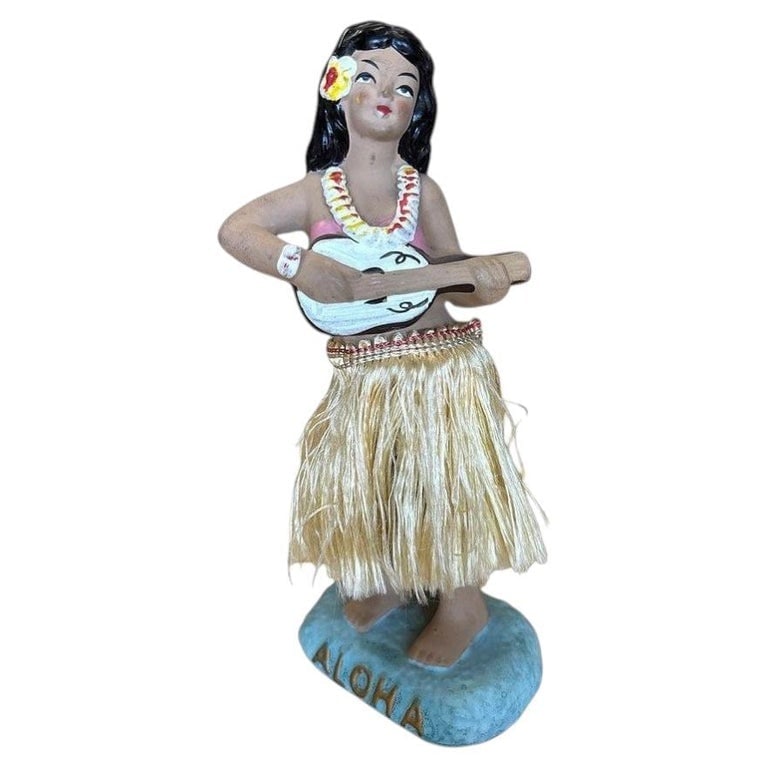 Mid-century "Aloha" Hula GirlCeramic Figurine w/ Ukulele and Red Flowers: Original post-war ceramic chalk-ware dancing Hawaiian Hula girl figurine made from lightweight plaster and painted in vibrant tropical colors and a fabric hula skirt. It depicts a young Hawaiian hula