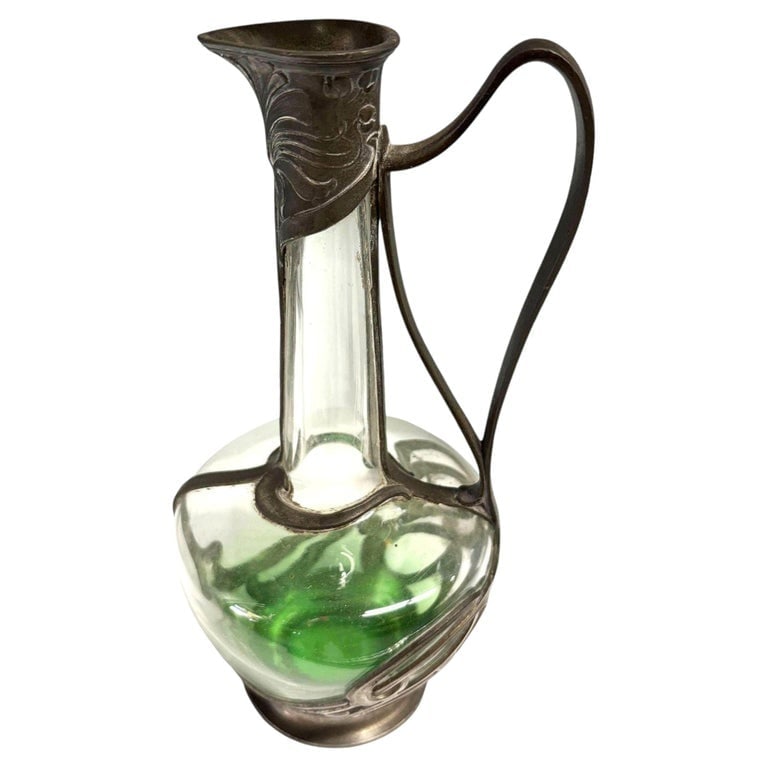 Austrian Art Nouveau Pewter Jugendstil Clade Green Art Glass Wine Carafe: A striking example of early 20th-century Jugendstil design, this elegant Wine Carafe features a vibrant emerald green glass liner encased in a sweeping, stylized pewter mount. The metalwork showcases