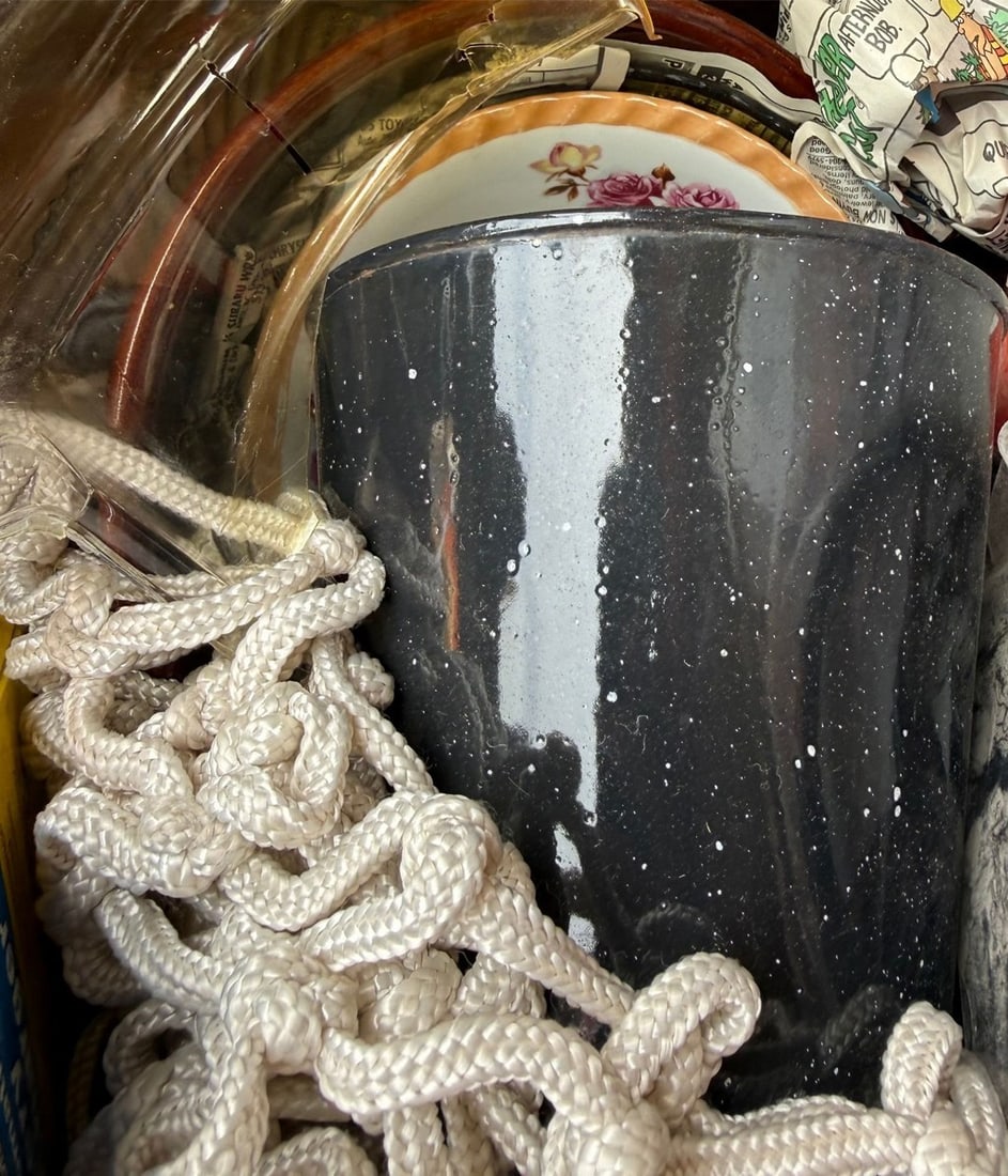 Collection of Vintage Kitchenware and Basketball Net: A varied collection including a speckled enamelware pot, a porcelain saucer with a floral motif, and a basketball net made of woven synthetic rope. The enamelware pot is dark grey/blk with white speck
