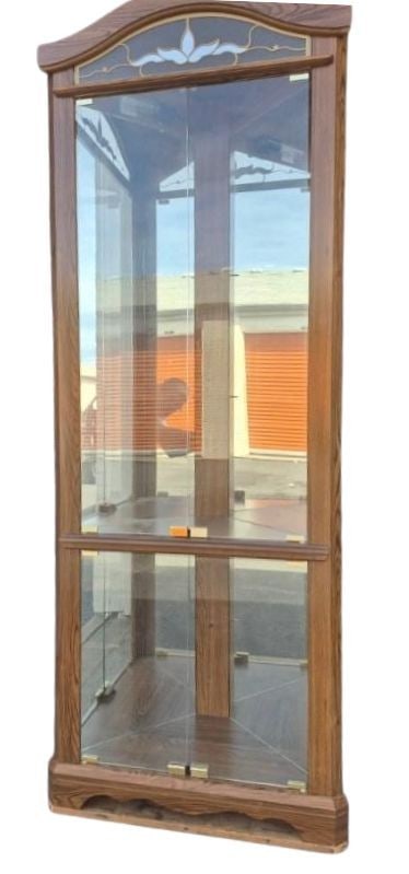 Traditional Style Lighted Curio Cabinet: This traditional style curio cabinet features a warm oak finish, an arched pediment with decorative scrolling, and glass doors opening to three interior glass display shelves. The cabinet is lighted,