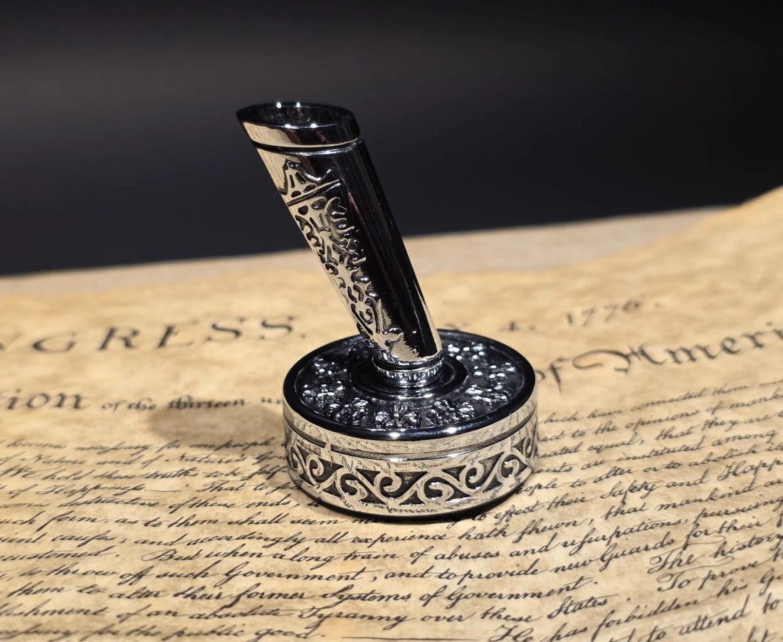 Silver Metal Single Fountain or Dip Pen Holder: 1 3/4" tall. A vintage-style silver metal pen holder with raised decorative detailing and an angled sleeve for holding a fountain pen or dip pen. The engraved patterns and weighted base give it a clas