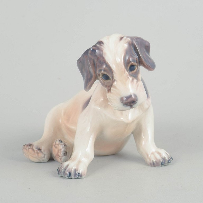 Dahl Jensen, Denmark. Porcelain dog figurine in muted tones with brown-grey accents. Approx. 1930s.: Dahl Jensen, porcelain dog figurine. Naturalistically modelled porcelain figure of a seated dog with soft forms and finely detailed features. Glazed in muted tones with brown-grey accents. Model 1008.