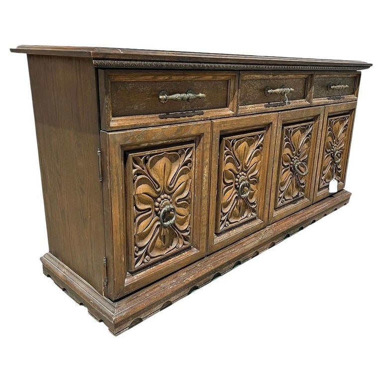 Mid Century Mediterranean Revival Carved Oakwood Buffet Cabinet: Mid-century Mediterranean Revival dining room buffet crafted with exquisitely carved drawer/cabinet fronts. Its elevated stature features brass drawer pulls and duel fold cabinet doors with floral mot
