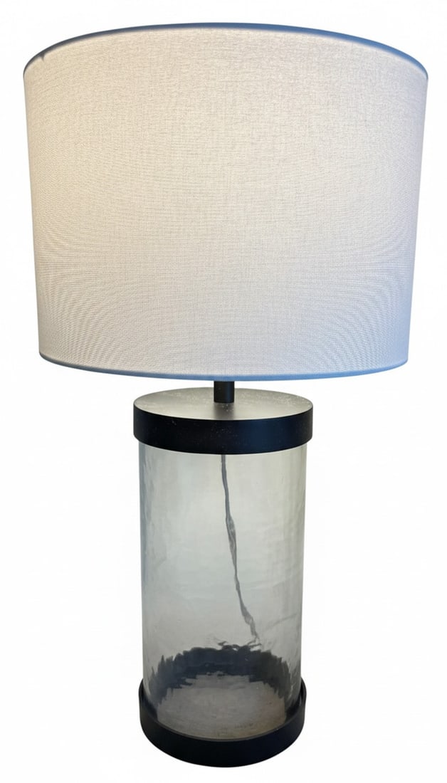 Modern Glass and Metal Cylinder Table Lamp with Linen Shade: A modern table lamp featuring a clear hammered glass cylinder body with black metal accents at the top and base. It is topped with a white linen drum shade with a light blue trim, providing a contempo