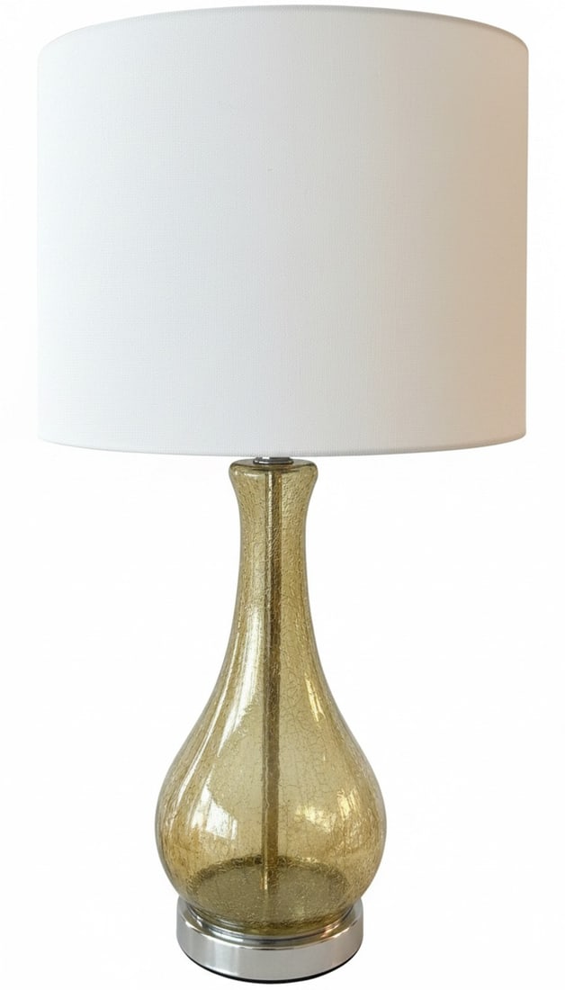 Contemporary Crackle Glass Table Lamp with White Shade: A contemporary table lamp featuring a crackle glass base in an amber hue, resting on a polished silver-tone metal foot. It is topped with a drum-shaped white fabric shade. The lamp adds a touch of mod