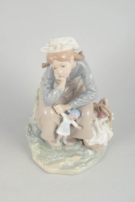 Lladró,, Spain. Porcelain figurine of a seated girl with doll in pastel tones. Approx. 1980s. - 2