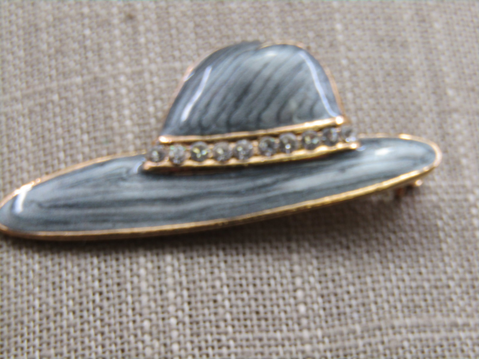 Enameled & Rhinestone Ladies' Hat Brooch 2": Title: Enameled & Rhinestone Ladies' Hat Brooch 2" Description: Enameled & Rhinestone Ladies' Hat Brooch 2" by 1", offset brim with a rhinestone band and gold tone frame and undercarriage.