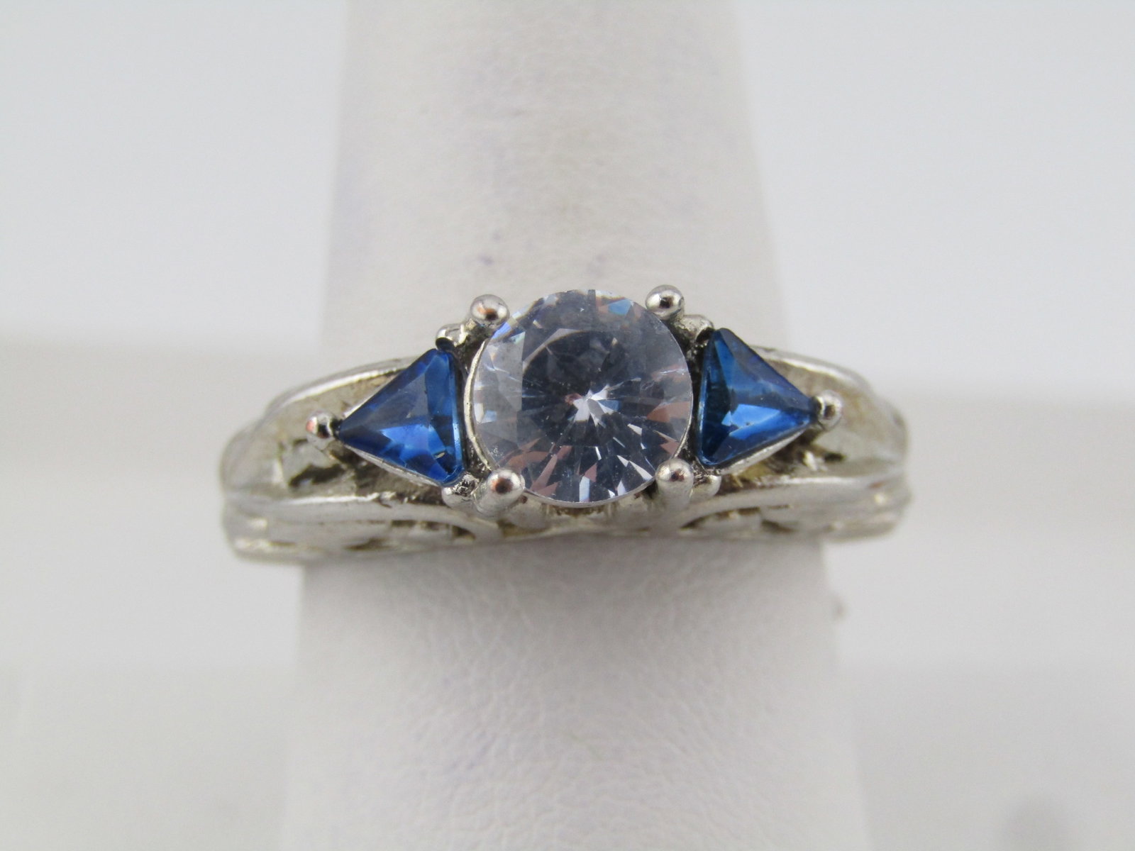 Silver Tone Blue & Clear Ring, Sz. 9, High Scrolled, 1990's: Title: Silver Tone Blue & Clear Ring, Sz. 9, High Scrolled, 1990's Description: Silver Tone Blue & Clear Ring, Sz. 9, High Scrolled, 1990's. This is a costume ring with a 7mm r ound clear stone in the