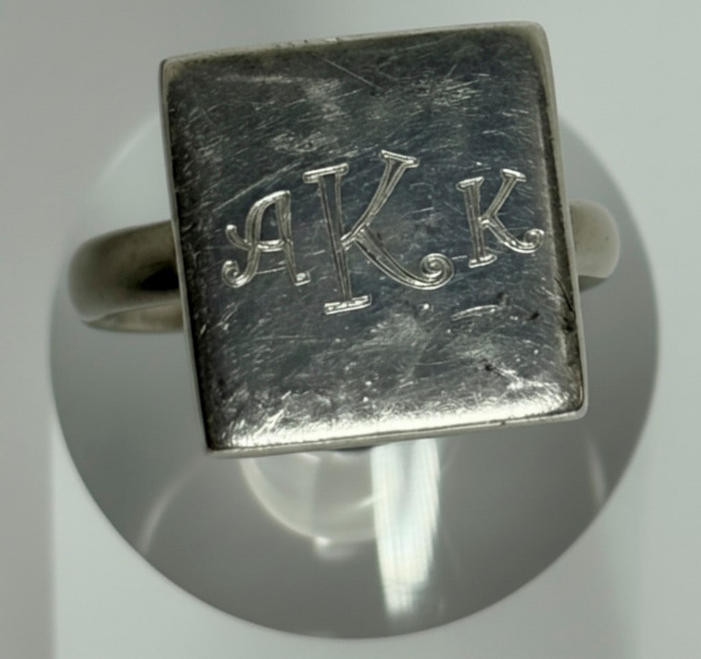 Sterling Silver Monogrammed Signet Ring: A sterling silver signet ring featuring a square-shaped top, engraved with the initials "AKK". The ring has a simple band and shows some wear consistent with age. Jewelry Type: Ring Metal: Sterling