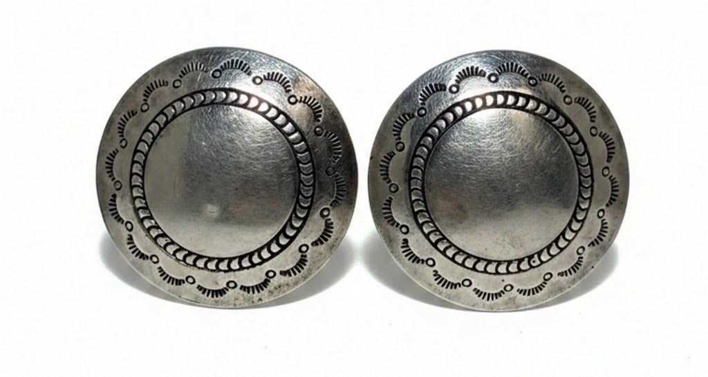 Sterling Silver Domed Disc Earrings: A pair of sterling silver domed disc earrings featuring a central raised dome surrounded by a textured border with repeating crescent and dot motifs. The earrings have posts for pierced ears. The desi