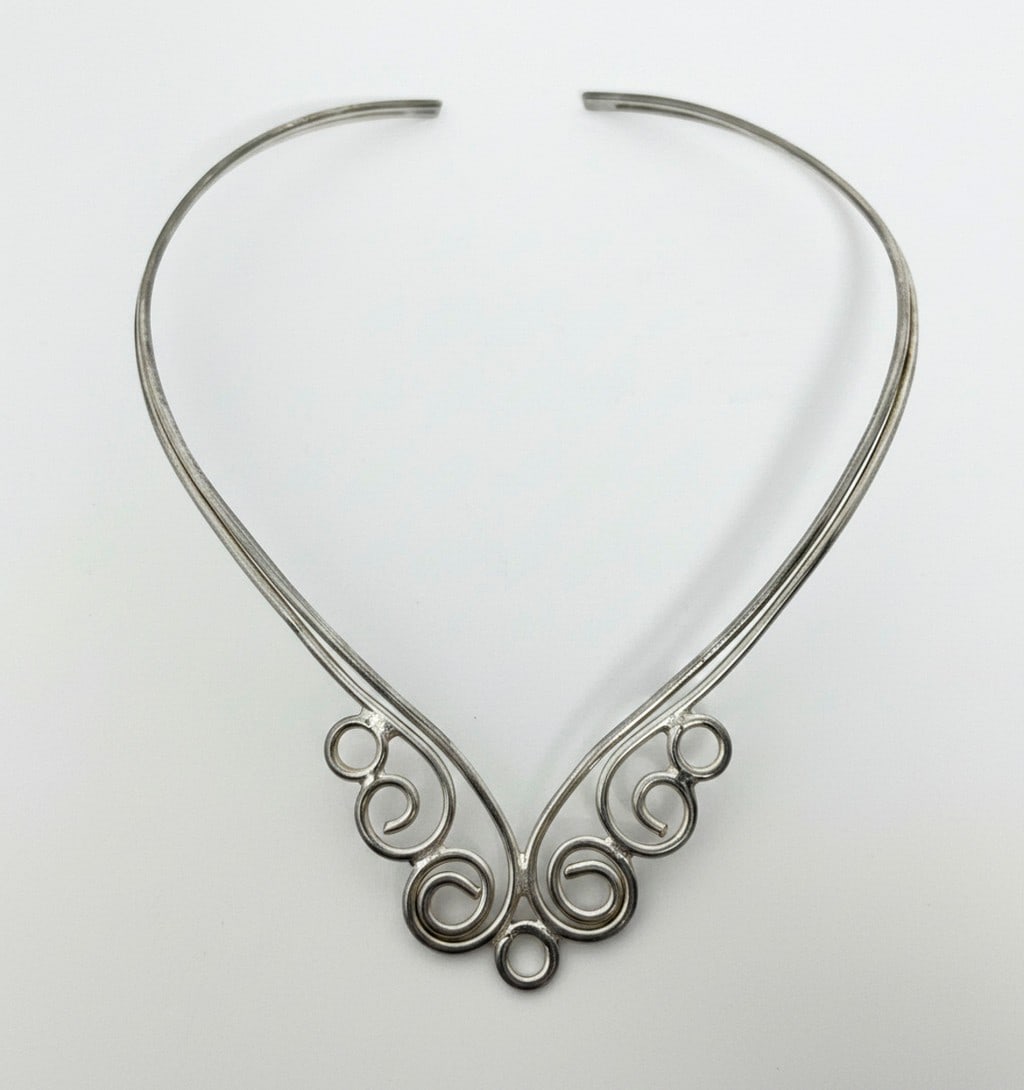 Sterling Silver Scrollwork Choker Necklace: This vintage choker necklace features a graceful scrollwork design crafted from sterling silver. The rigid collar style is open at the back for easy wear, and the decorative front element showcases
