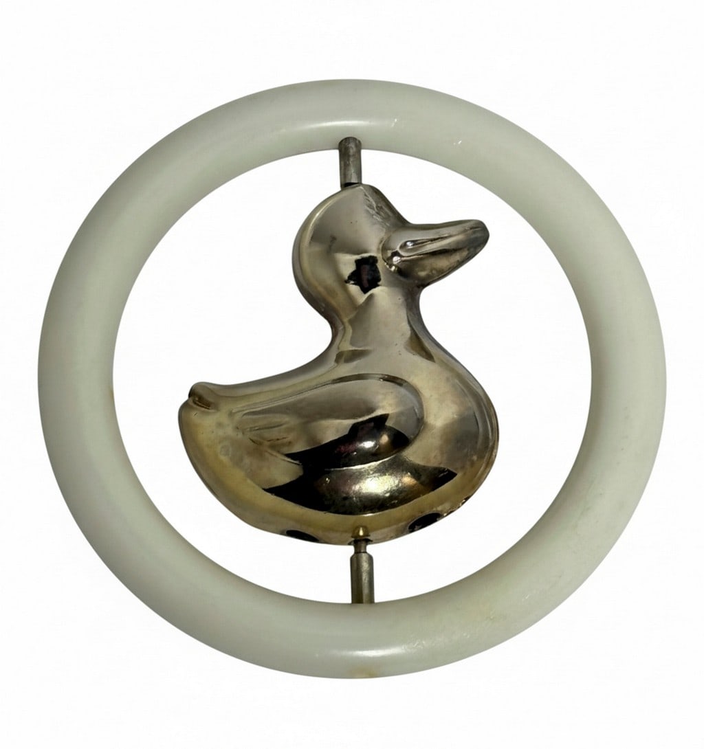 Silverplated Duck Baby Rattle: A vintage silverplated baby rattle featuring a charming duck figure suspended within a white plastic ring. The duck is polished to a shine and the rattle produces a gentle sound. The item comes in