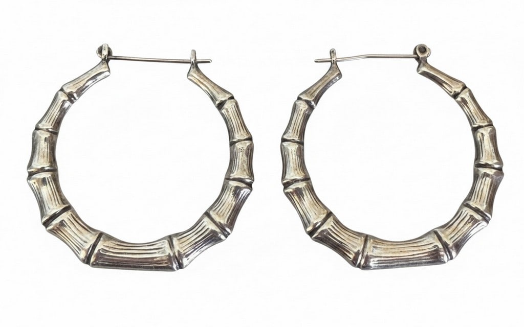 Sterling Silver Bamboo Motif Hoop Earrings: A pair of sterling silver hoop earrings designed with a bamboo motif. The earrings feature a hinged post closure. The silver has a slightly darkened patina in the recesses, enhancing the bamboo