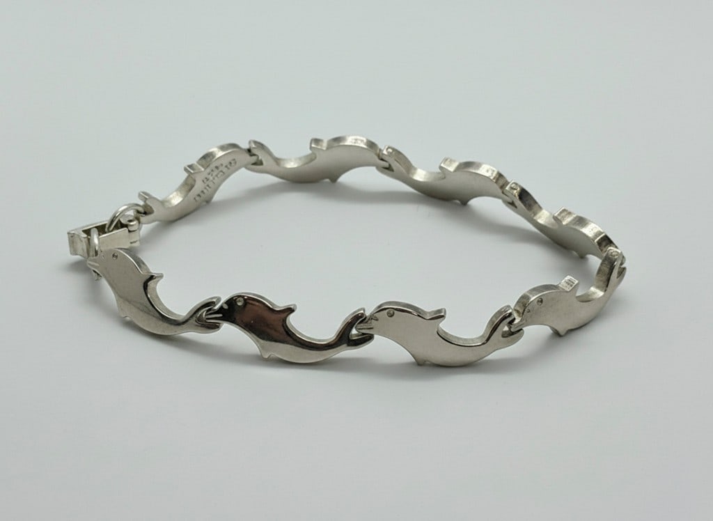 Sterling Silver Dolphin Link Bracelet: This charming bracelet features a series of sterling silver links, each sculpted in the form of a leaping dolphin. The dolphins are interconnected, creating a fluid and graceful design. The bracelet