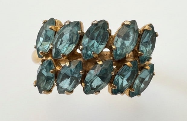Vintage Blue Topaz-Like Marquise Cluster Ring: This vintage ring features a striking cluster of marquise-cut blue topaz-like stones, arranged in two rows. The stones are set in what appears to be yellow prongs on a white metal band, possibly