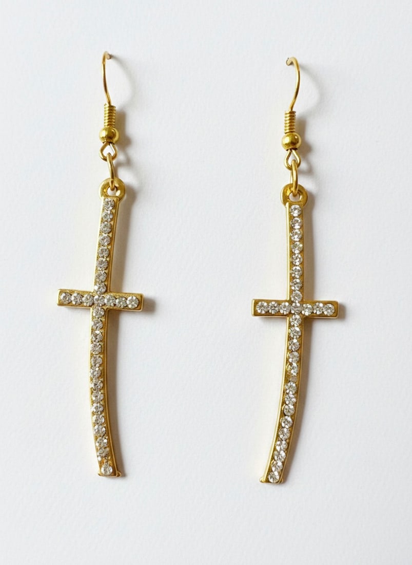 Gold-tone Dangle Earrings with Clear Rhinestones: A pair of gold-tone dangle earrings, each featuring a stylized cross design adorned with small, round, clear rhinestones. The earrings have a curved, sword-like shape with a horizontal bar forming