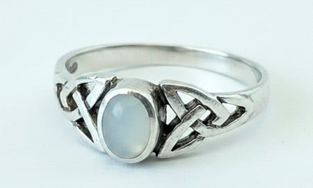 Sterling Silver Mother-of-Pearl Celtic Knot Ring: A sterling silver ring featuring an oval mother-of-pearl cabochon set within a Celtic knot design band. The intricate knot work forms the shoulders of the ring, leading to a smooth band. The