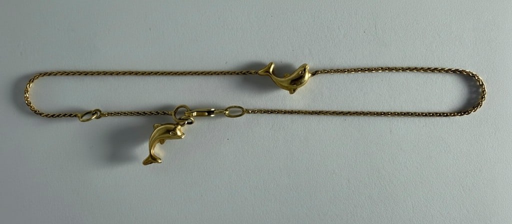 14k Yellow Gold Dolphin Charm Bracelet: This charming bracelet features a delicate foxtail chain crafted from 14k yellow gold, adorned with two playful dolphin charms. A spring ring clasp secures the bracelet, which also bears a visible