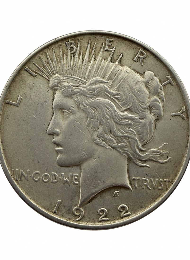 1922 US Peace Silver Dollar Coin: This is a 1922 US Peace Silver Dollar coin. The obverse features the head of Lady Liberty, depicted with a radiate crown. The reverse displays an eagle at rest on a rock, clutching an olive branch.