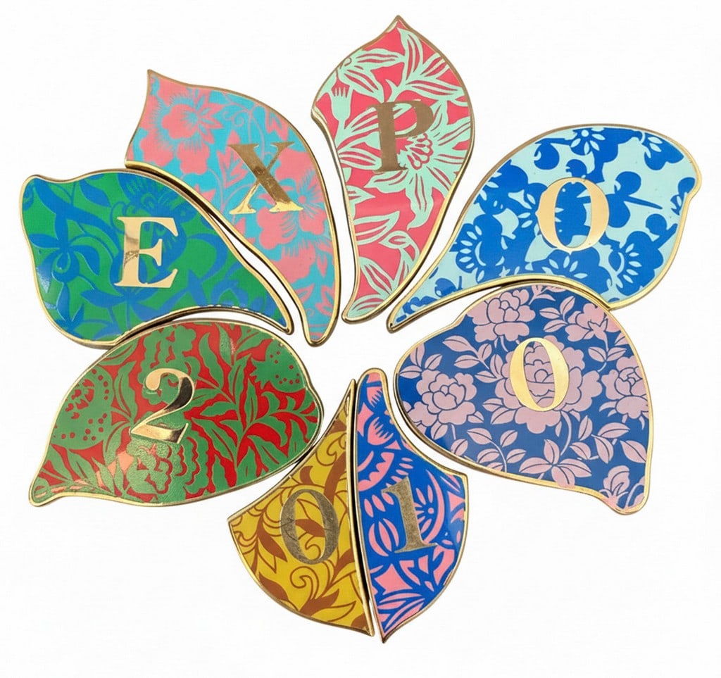 Expo 2010 Shanghai China Pin Set: A set of eight colorful, leaf-shaped pins with various floral patterns and letters/numbers reading "EXPO 2010". The pins are made of zinc alloy and were produced under the authorization of the Bureau