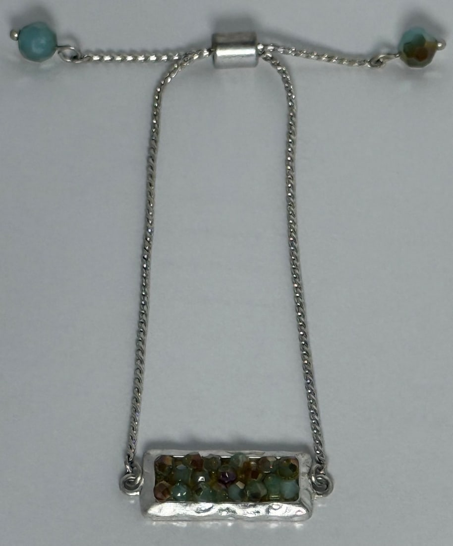 Silver and Faceted Bead Bolo Bracelet: This contemporary bolo bracelet features silver color bar set with multiple small, faceted green and brown beads. The bracelet has an adjustable sliding clasp with a single faceted greenish-blue bead