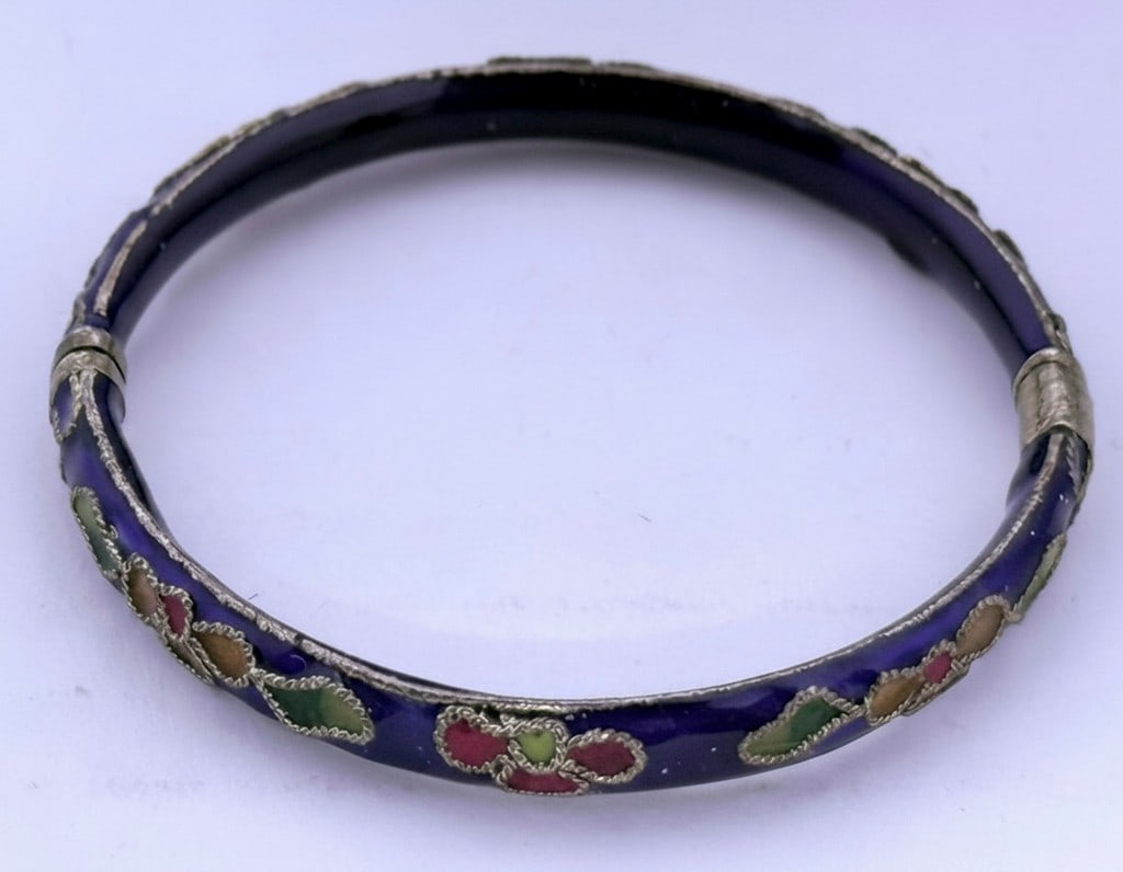 Cloisonne and Silver Bangle Bracelet: This bangle bracelet features a dark blue cloisonne enamel background with a repeating floral motif in red, green, and orange enamels. The metal appears to be silver, with intricate detailing around