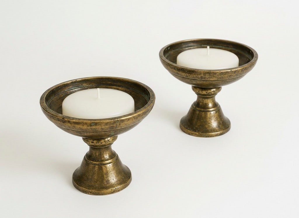 Pair of Antique Brass Pedestal Bowls / Candle Holders: A pair of antique brass pedestal bowls, likely used as candle holders, featuring a deep, aged patination. The bowls have a classic, simple form, with a wide, shallow basin resting on a flared