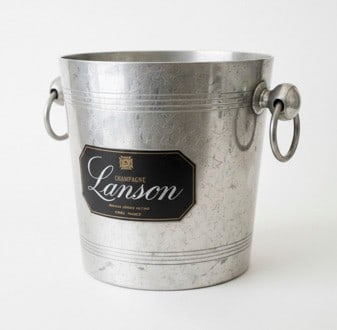 Vintage Lanson Champagne Ice Bucket: A vintage Lanson Champagne ice bucket, likely aluminum or silver-plated, with a textured finish and two ring handles. The front features a black label "CHAMPAGNE Lanson MAISON FONDÃ‰E EN