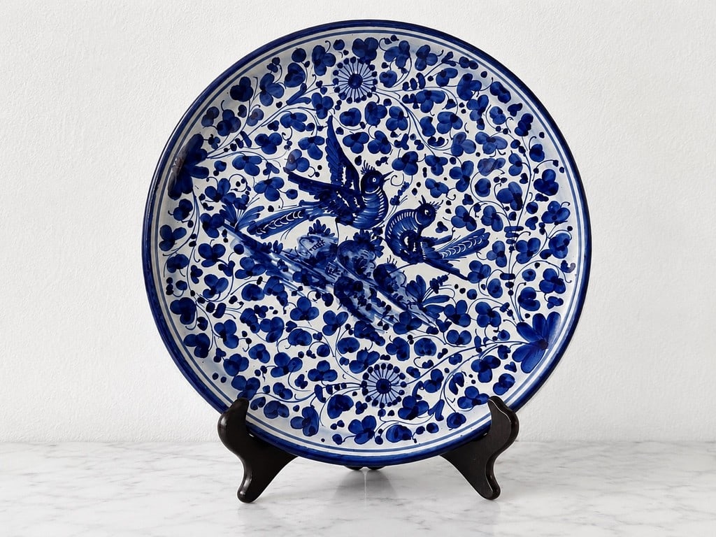Blue and White Hand-Painted Charger with Birds and Foliage: A decorative ceramic charger plate, hand-painted in vibrant cobalt blue and white with a central motif of two birds amidst scrolling foliage and floral patterns. The design is reminiscent of