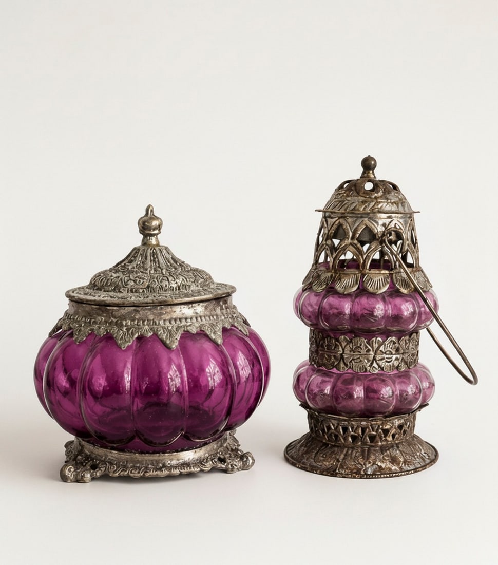 Pair of Decorative Purple Glass and Metal Containers: This lot features two ornamental items with purple glass and ornate silver-toned metalwork. One is a lidded jar with a domed, intricately patterned metal lid and base, housing a ruffled purple glass