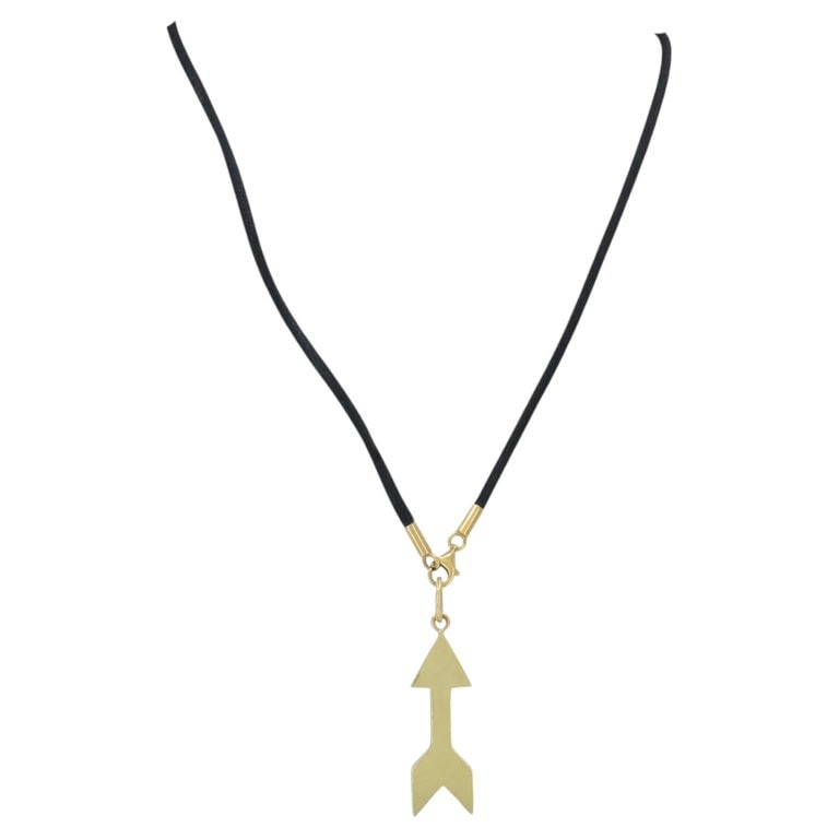 Cartier 18k Gold Arrow Pendant Black Silk Cord Necklace: Cartier 18k yellow gold arrow pendant necklace, circa 1990s, designed with a flat stylized arrow pendant suspended from a black cord necklace. The pendant has a clean graphic form with a pointed