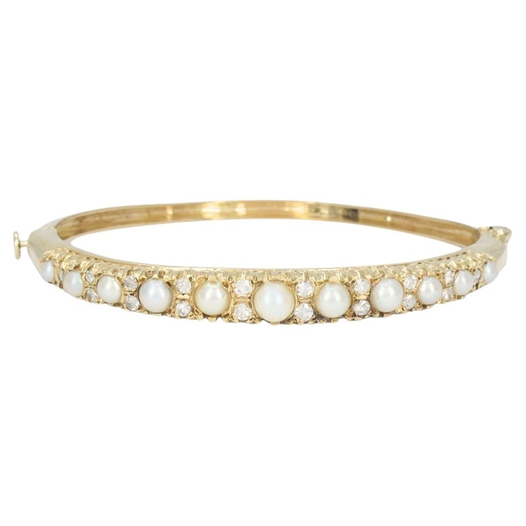 Antique Victorian 14k Yellow Gold Pearl Diamond Hinged Bangle Bracelet: Antique 14k yellow gold pearl and diamond hinged bangle bracelet, circa 1900. This bangle features a graduated row of pearls across the front, accented by diamonds set between each pearl for a