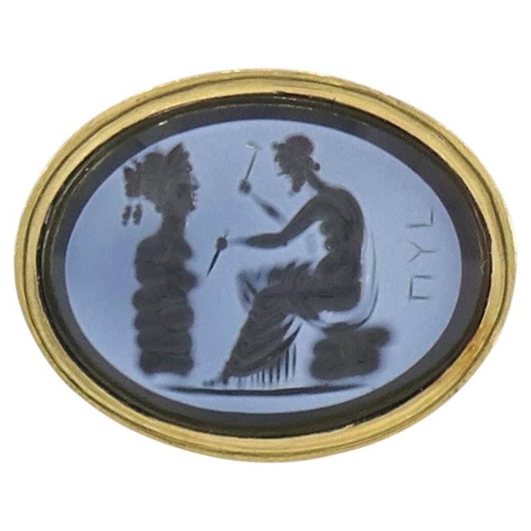 Vintage 18k Gold Hardstone Intaglio Signet Ring: This 18k yellow gold ring is set with an oval black and white hardstone intaglio, depicting a classical male sculptor at work. The finely engraved scene shows the figure seated as he carves a