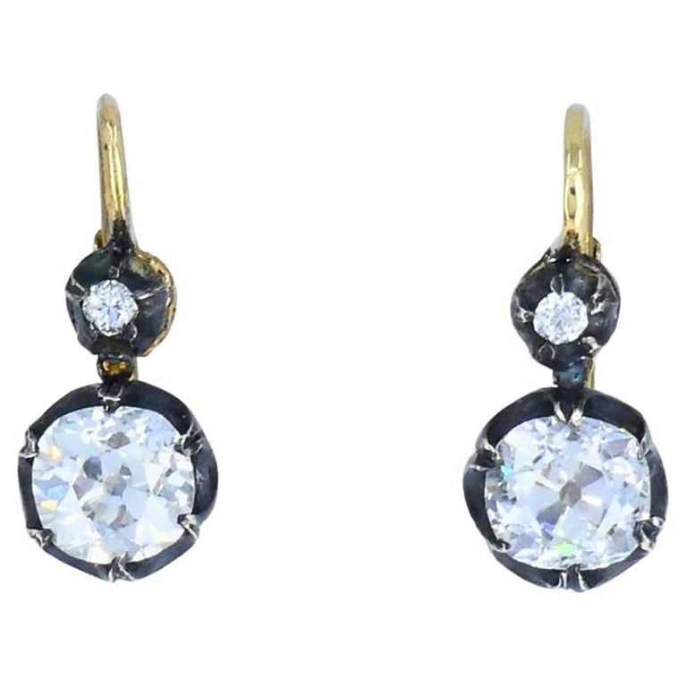 Victorian 14k Gold Silver Two-Stone Diamond Earrings Old Mine Cut, Antique: This pair of Victorian two-stone diamond earrings is crafted in 14k yellow gold with silver settings. Each earring is designed with a small top diamond and a larger suspended diamond below, creating a