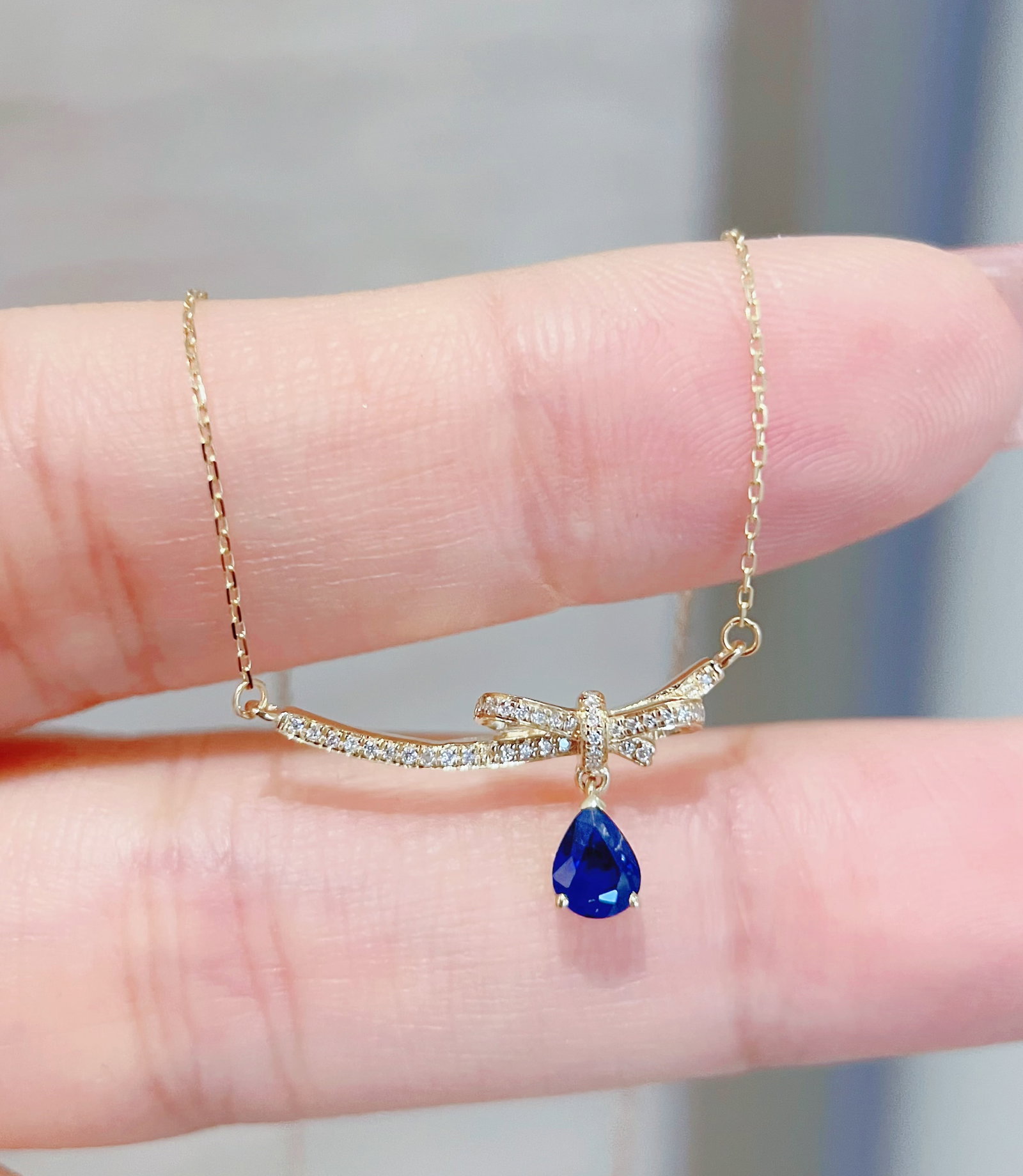 18K Gold Natural Sapphire Necklace: Title: 18K Gold Natural Sapphire Necklace Description: The diamond bow elegantly curves along the collarbone, with a drop of deep ocean blue sapphire. It ties the girl's secrets and the serene deep bl