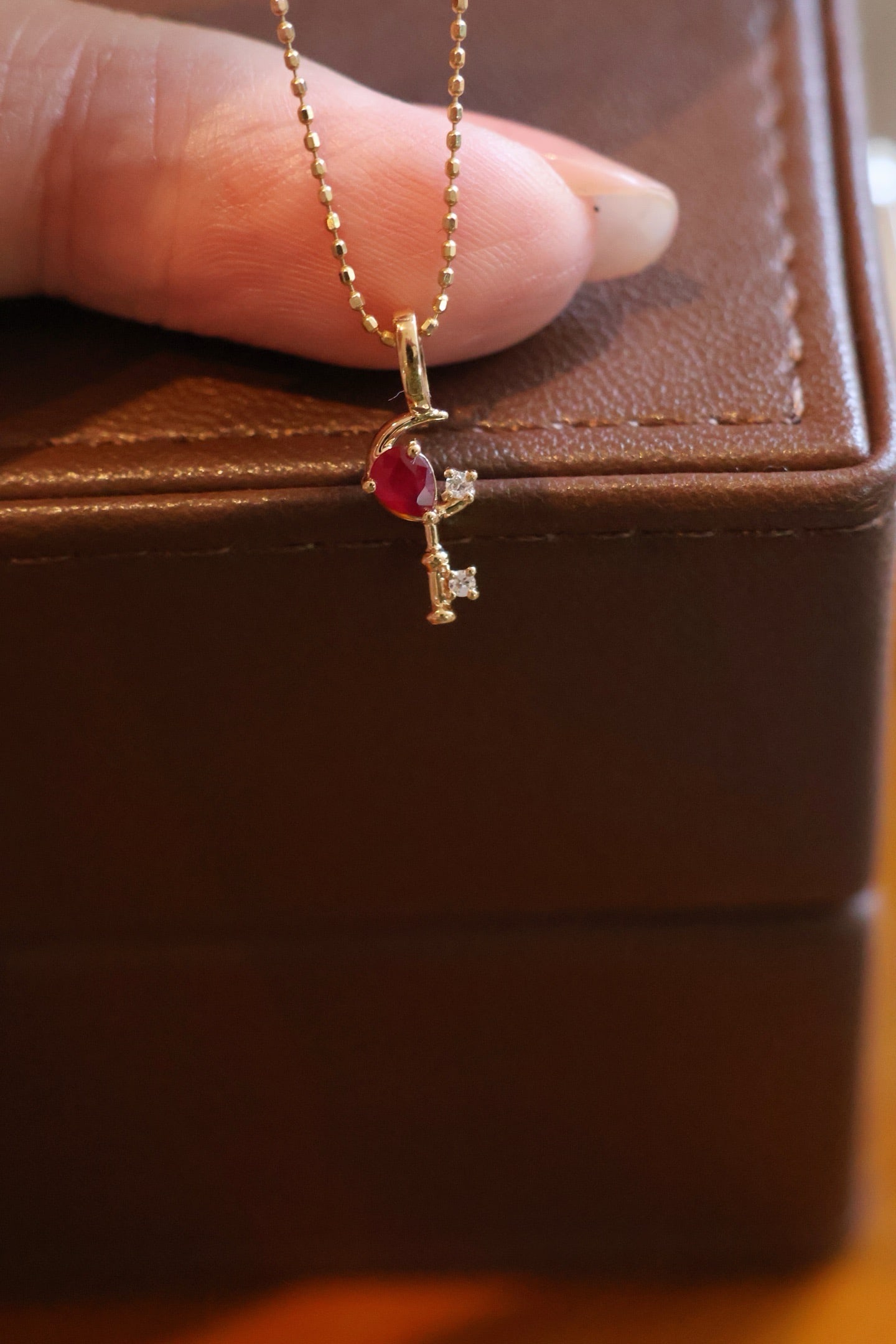 18K Gold Ruby Diamond Pendant: Title: 18K Gold Ruby Diamond Pendant Description: This crescent-shaped key pendant is set with a teardrop ruby, complemented by two small diamonds, exquisite and full of ingenuity. Its versatile