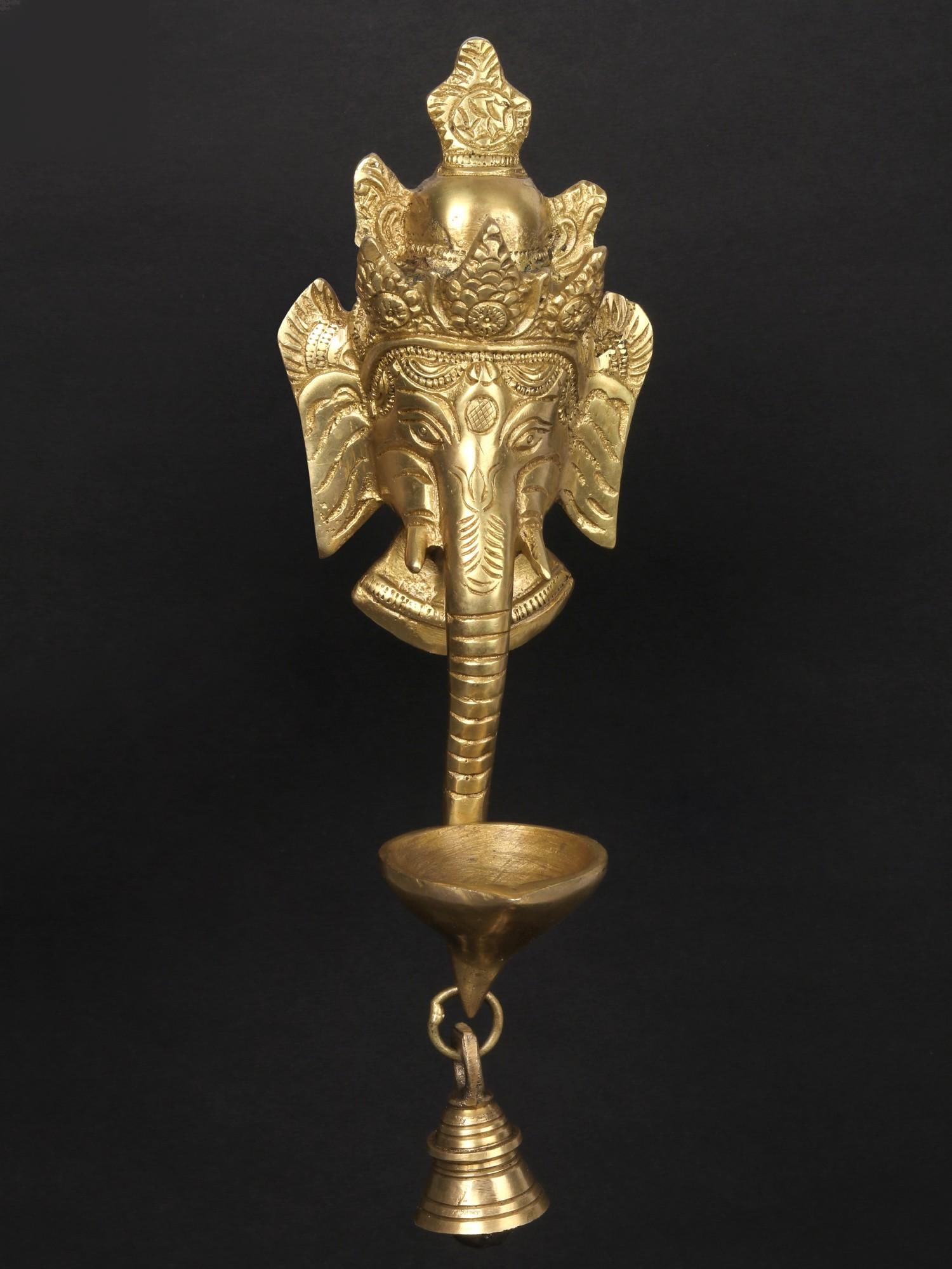 11" Lord Ganesha Wall Hanging Mask with Brass Diya and Bell | Handmade | Made in India: Description: See It In Your Home In every work of art, the spirit of its creator lives on." - Ancient Proverb The statue crafted by skilled hands in India, this brass wall-hanging mask of Lord Ganesha