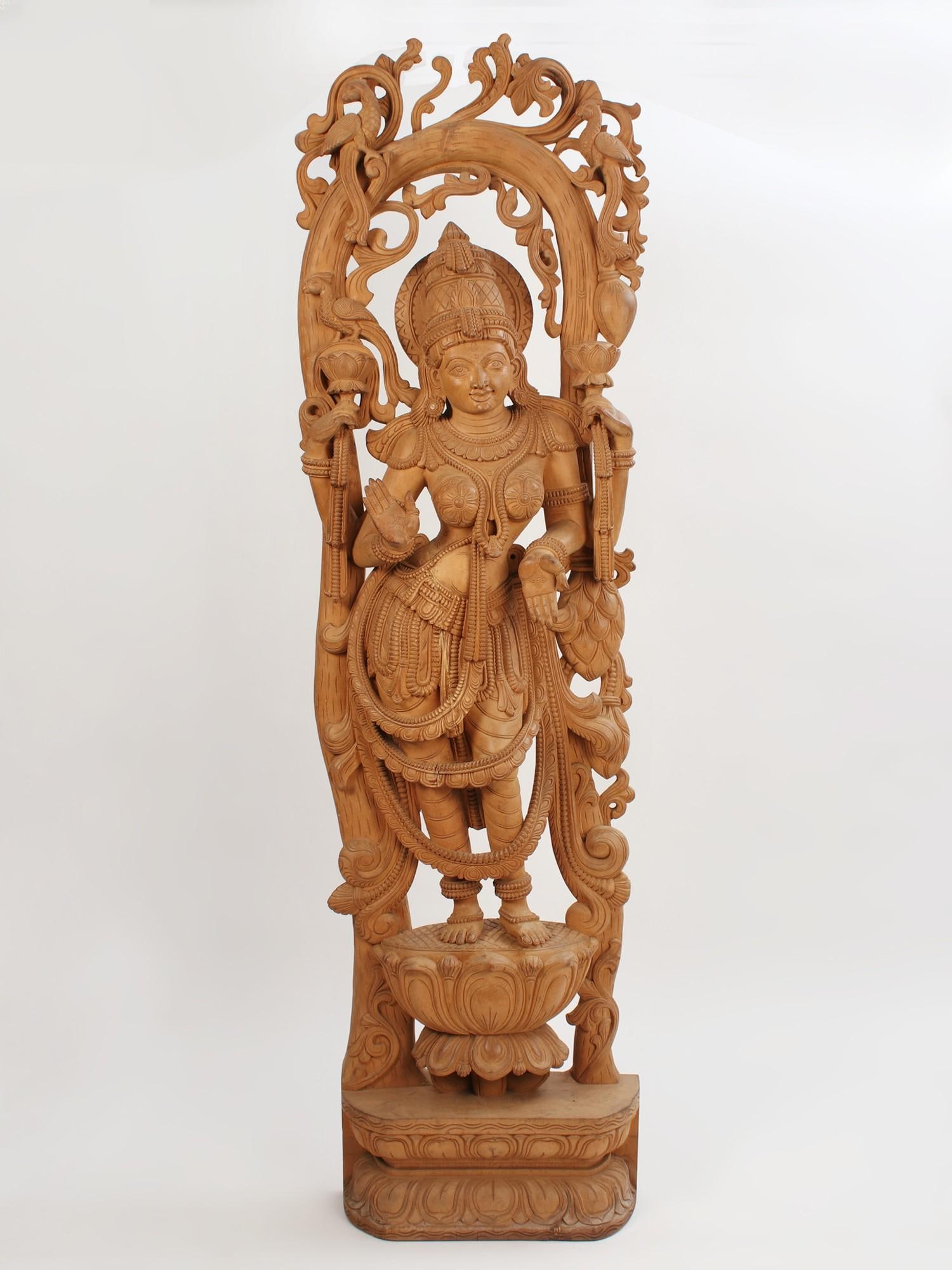 76" Superfine Large Wooden Standing Goddess Lakshmi On Lotus Pedestal: Description: The divyaroopa of Lakshmi Devi, captured in organic wood medium. The Lakshmi statue that you see on this page depicts the wife of Vishnu in the cosmic (‘divya’) glamour of Her