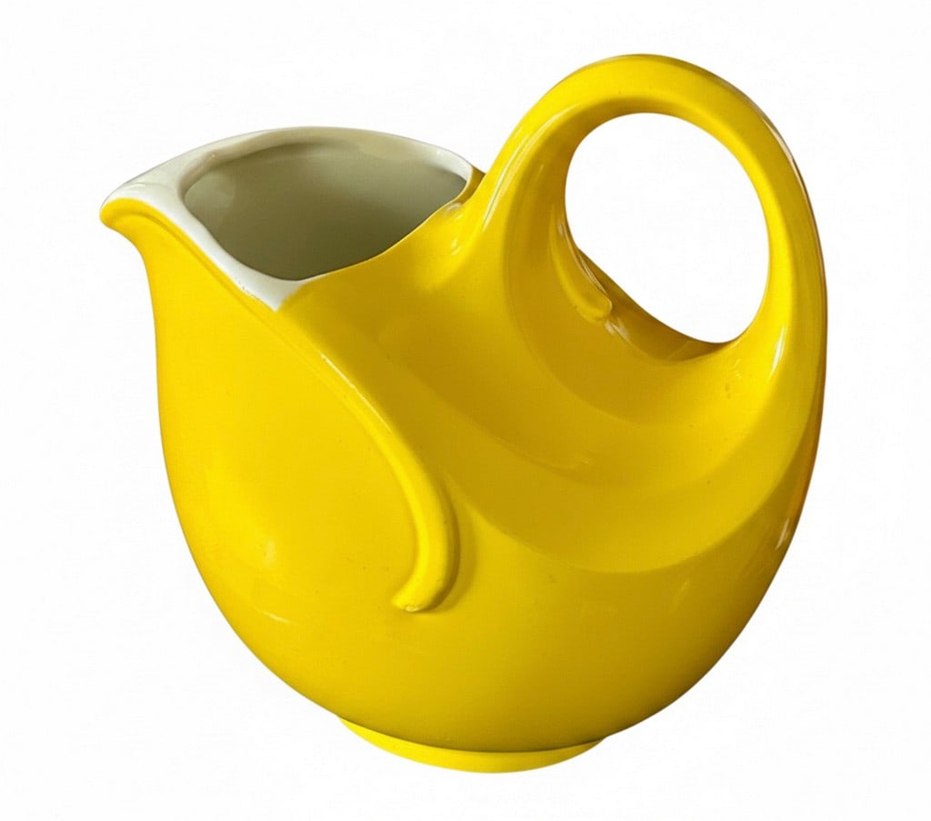 Vintage Mid-Century Yellow Ceramic Pitcher: A vibrant yellow ceramic pitcher with a distinctive curved handle and spout, likely from the mid-20th century. The interior is white. The design suggests a mid-century modern aesthetic, suitable for