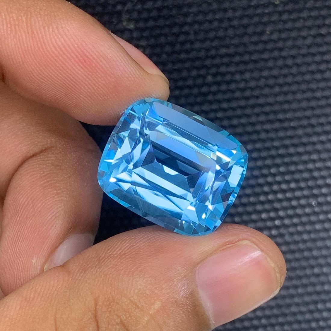 Swiss Blue Topaz Gemstone: 35.65 Carat Cushion Cut, Eye Clean: Introducing a magnificent Swiss Blue Topaz gemstone. Its long cushion shape, which sparkles wonderfully, stands for prosperity and love. This jewel is exquisitely carved and emanates grace and charm. 