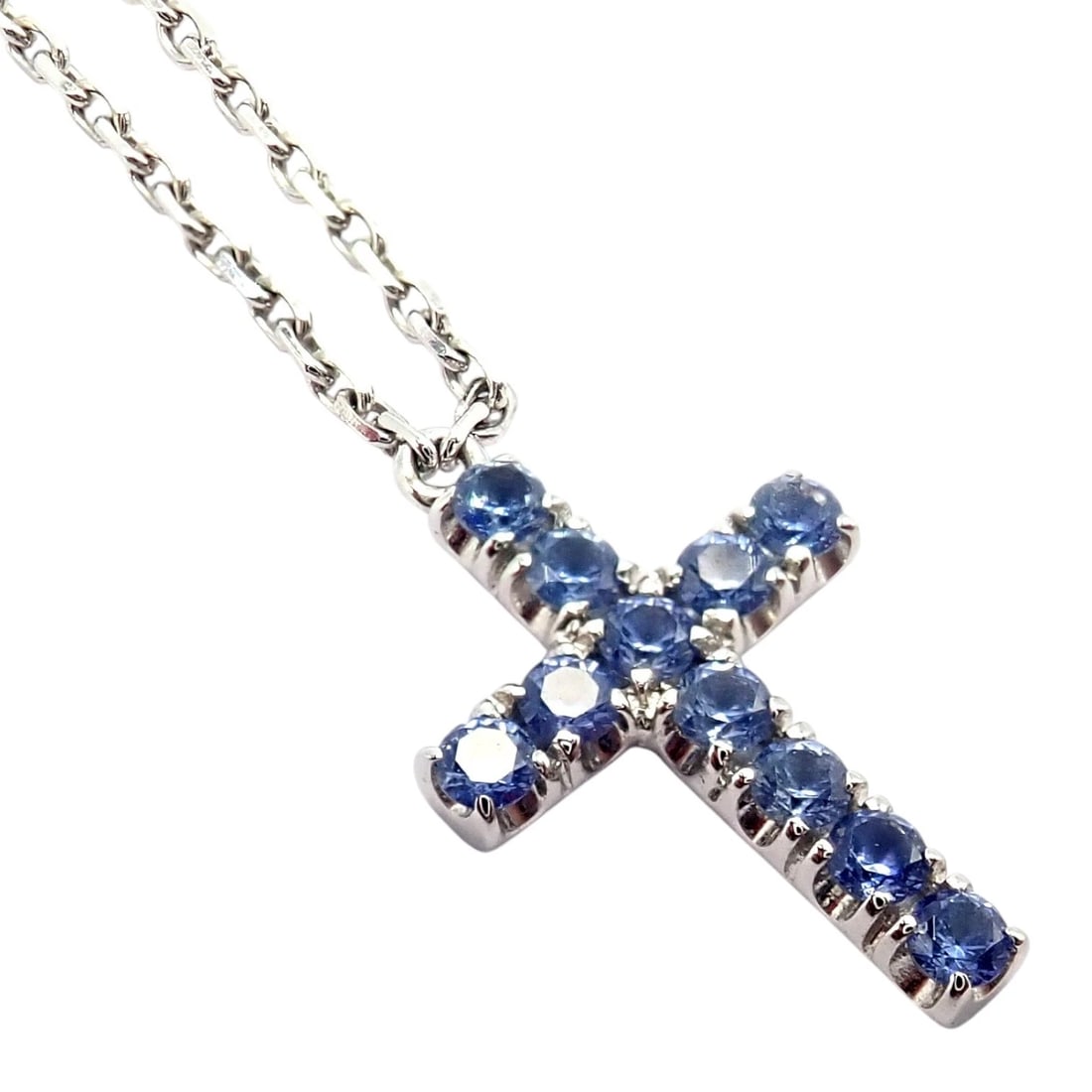 Authentic! Cartier 18k White Gold Sweet Cross Blue Sapphire Pendant Necklace: Elegant Cartier Sweet Cross necklace crafted in 18k white gold, featuring a delicate cross pendant set with vibrant round blue sapphire gemstones. The cool blue hues create refined sparkle against the