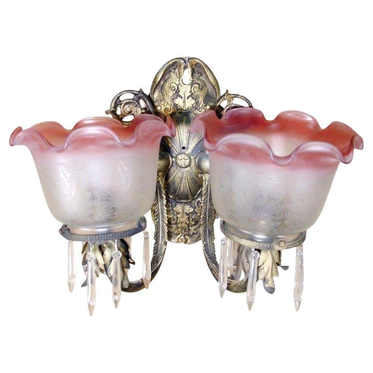 Neoclassical Brass Sconce With Acid Etched Rose Shades: Neoclassical wall sconce featuring a pair of feathered brass arms extending from a floral motif wall mount. The floral motif continues throughout the piece. The sconce features a pair of acid etched r